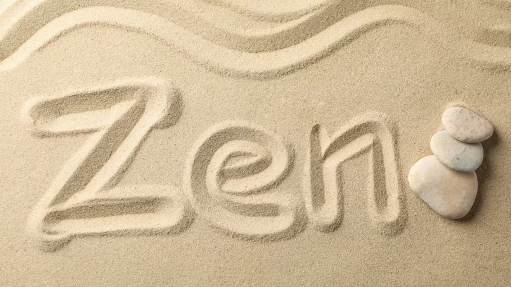 Zen escrito em areia, com pedras ao lado - ambos elementos relacionados a filosofia zen budista